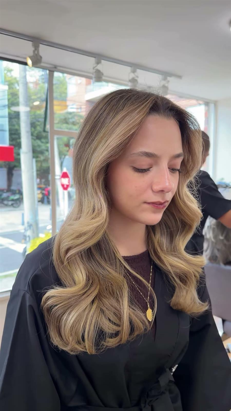 Clienta con balayage rubio en ondas junto a la ventana del salón